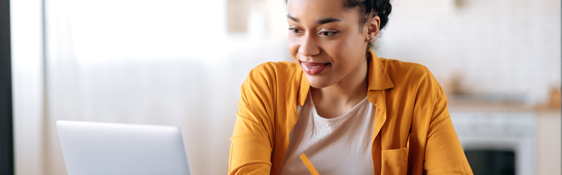 Woman working at desk smiling at laptop and writing on a notepad
