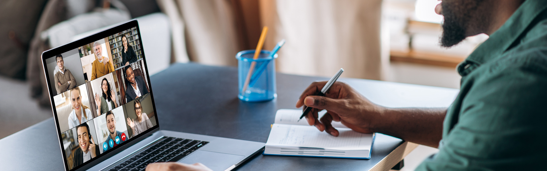 Man sat at desk on virtual video-call and taking notes