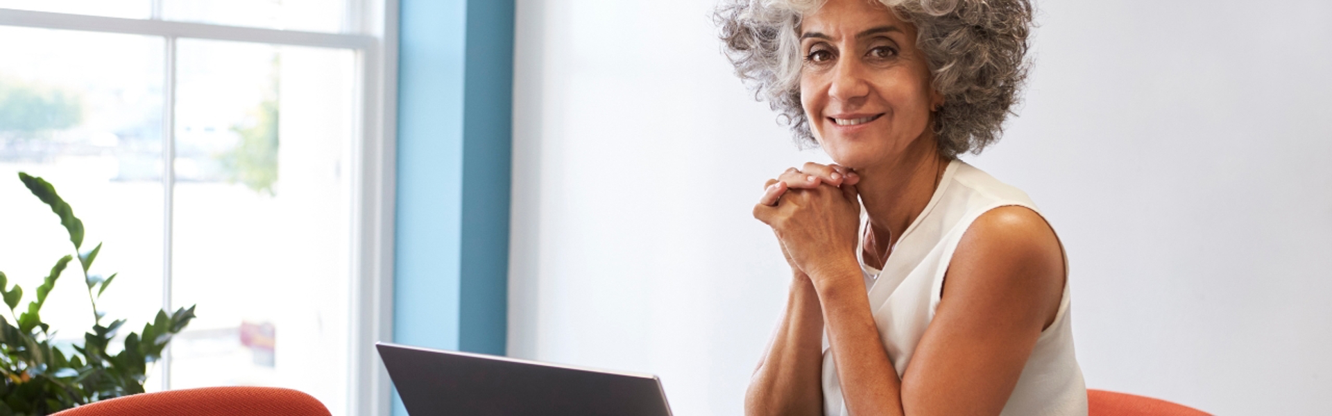 Woman working at desk smiling at camera with hands together